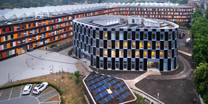 Im Bild ein rundes Gebäude mit Photovoltaik an der Fassade, der klimaneutrale Erweiterungsbau vom Umweltbundesamt, bei dem es sich um ein Plus-Energie-Gebäude handelt.