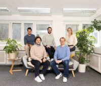 Ein Team von vier Männern und einer Frau platzieren sich leger auf einem Sofa.