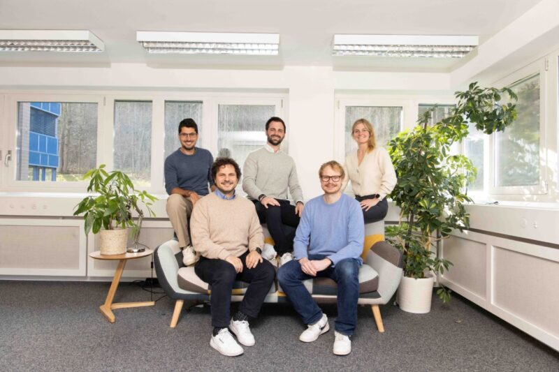 Ein Team von vier Männern und einer Frau platzieren sich leger auf einem Sofa.