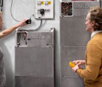 Zwei Personen stehen an einem Batterieschrank von Varta.