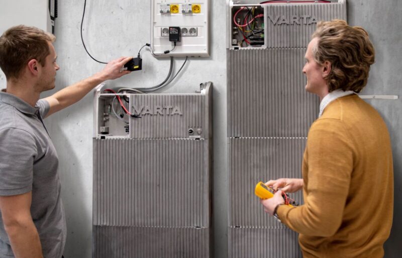 Zwei Personen stehen an einem Batterieschrank von Varta.