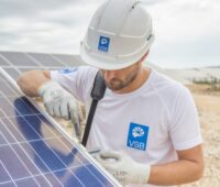 Mann mit VSB-Logo montiert Photovoltaik-Modul auf einer Freifläche.