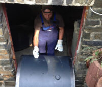 Zylinderförmiges Speichersegment wird von einem Handwerker durch eine schmale Kellertür bugsiert