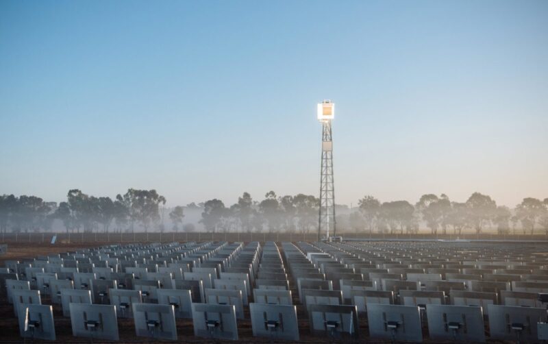 Gitterturm vor blauem Himmel, Spiegel sind darauf ausgerichtet, die Turmspitze scheint zu leuchten: ein CSP-Turmkraftwerk.