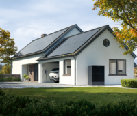 Das Bild zeigt ein weißes Einfamilienhaus, schräg von der Seite, rechts und links Bäume, mit Blick aus dem Grün, in der Garage ein PKW mit Wallbox und vor der Garage eine Wärmepumpe.