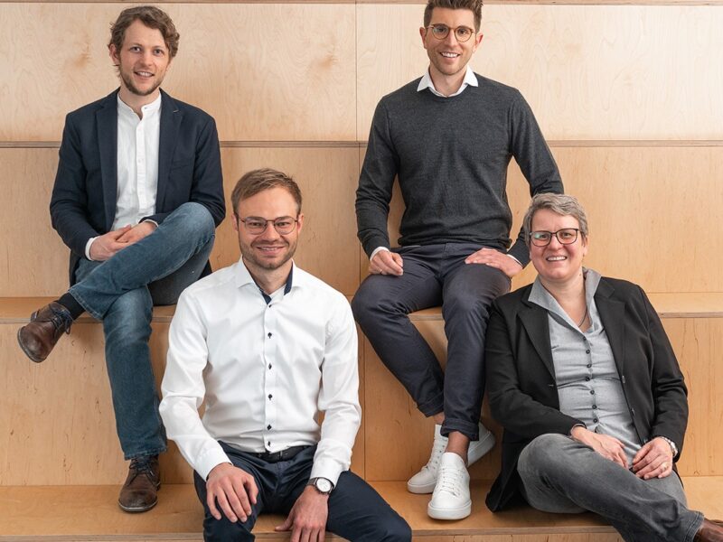 Vier Menschen auf Holzstufen - das Management-Team von Voltstorage will Redox-Flow-Batterien marktreif machen