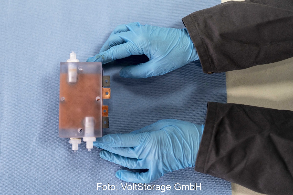 Zu sehen ist eine Batteriezelle der Iron-Redox-Flow-Stromspeichertechnologie, gehalten von Händen in blauen Handschuhen.