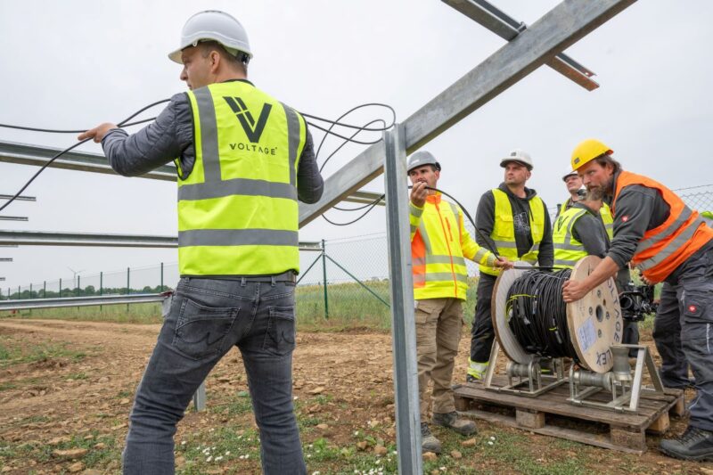 Arbeiter in Sicherheitswesten verlegen Kabel in einem PV-Park.