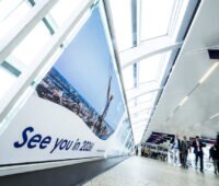 Besucherinnen und Besucher gehen durch einen hellen Verbindungsgang der Hamburg Messe. Auf einer großen Wandgrafik steht „See you in 2026!“.