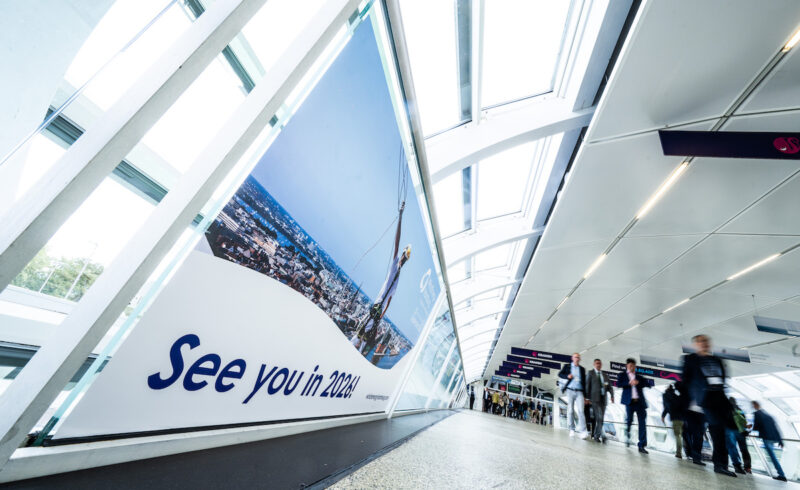 Besucherinnen und Besucher gehen durch einen hellen Verbindungsgang der Hamburg Messe. Auf einer großen Wandgrafik steht „See you in 2026!“.
