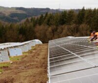 Arbeiter montieren eine Freiflächenanlage auf hügeligem Terrain.