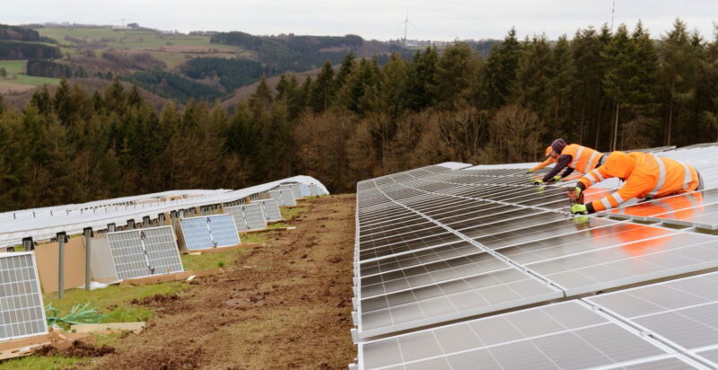 Arbeiter montieren eine Freiflächenanlage auf hügeligem Terrain.