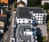 Luftbild einer städtischen Wohnstraße mit einem Gebäude, das PV auf dem Flachdach installiert hat.