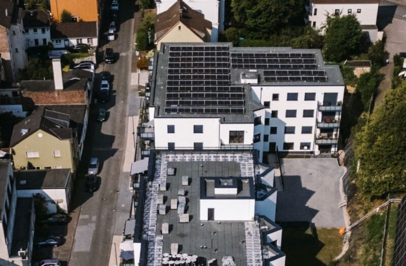 Luftbild einer städtischen Wohnstraße mit einem Gebäude, das PV auf dem Flachdach installiert hat.