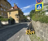 EIne Straße, an einer Mauer liegen Rohre für ein Wärmenetz.