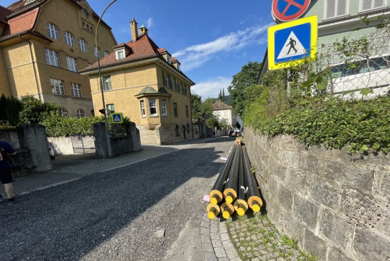 EIne Straße, an einer Mauer liegen Rohre für ein Wärmenetz.