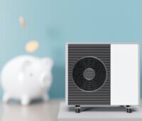 Das Bild ist ein Rendering und zeigt eine Wärmepumpe in dunkelgrau und weiß auf der rechten Seite scharf im Vordergrund, der Untergrund ist hellgrau, links daneben ein weißes Sparschwein unscharf im Hintergrund, beides vor einer unscharfen hellblauen Wand, in das Sparschwein fallen beige runde Kreise, die an Münzen denken lassen.