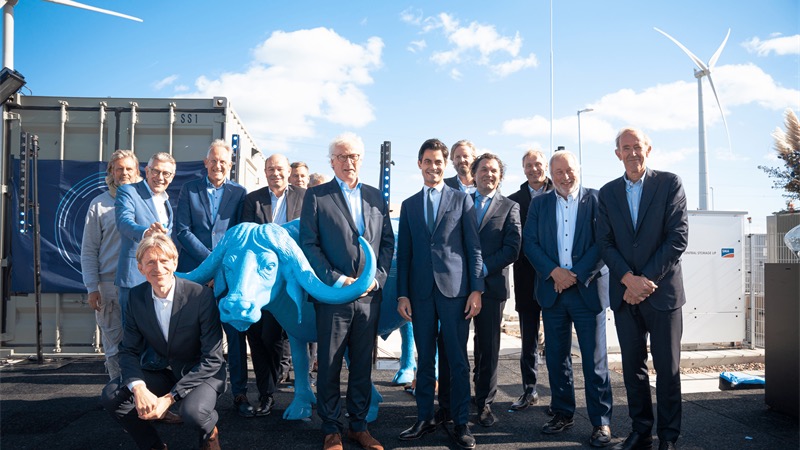 Eine Gruppe von Menschen, im Hintergrund Container und eine Windenergie-Anlage