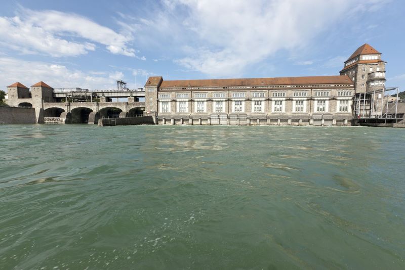 Ein altes Wasserkraftwerk am Rhein und bviel Wasserim Vordergrund.
