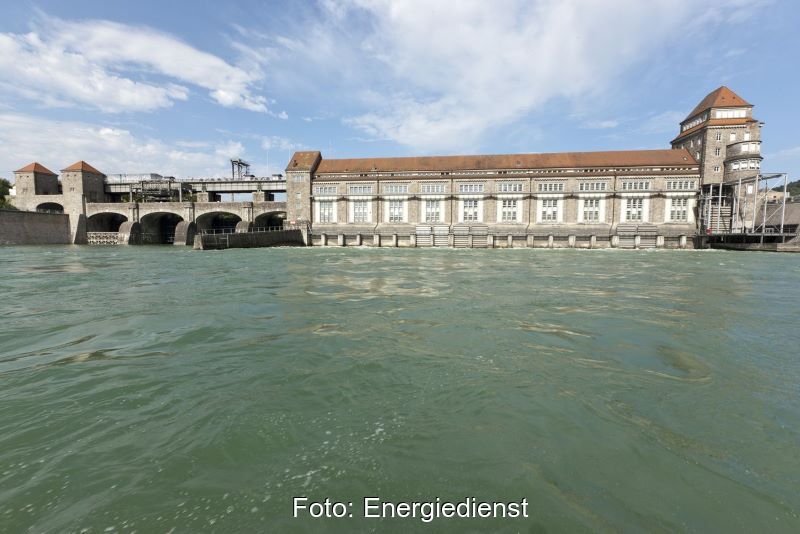 Ein altes Wasserkraftwerk am Rhein und bviel Wasserim Vordergrund.