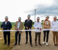 Sechs Menschen durchschneiden Band auf Feldweg, dahinter Windenergie-Anlage.