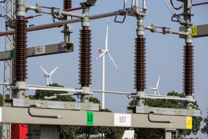 Zu sehen ist ein Umspannwerk der Wemag mit Windkraftanlagen im Hintergrund. Die Kosten für den Netzausbau müssen die Menschen in der Region und die Unternehmen dort tragen.