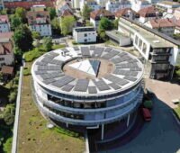 Luftbild eines runden Gebäudes mit Solarmodulen auf dem Dach.