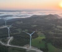 Windräder in Hügellandschaft aus der Luft mit Sonnenuntergang am Horizont.