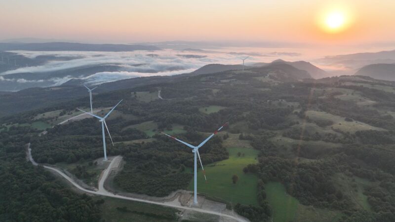 Windräder in Hügellandschaft aus der Luft mit Sonnenuntergang am Horizont.