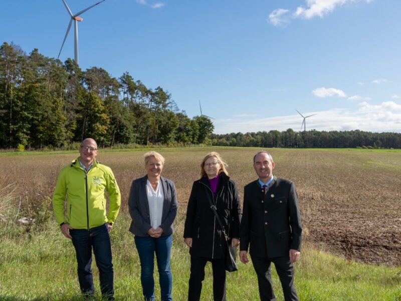 Zwei Männer und zwei Frauen, im Hintergrund drei Windenergie-Anlagen - Photovoltaik fehlt noch