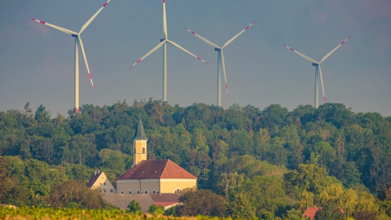 Windpark in Bayern, Zöschingen, drei Windenergie-Anlagen hinter einer Kirche. Symbol für Erneuerbare Energien.