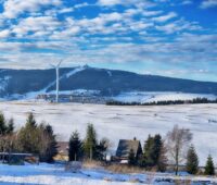 zwei Windenergie-Anlagen vor verschneiter Landschaft im Erzgebirge.