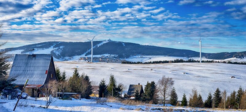 zwei Windenergie-Anlagen vor verschneiter Landschaft im Erzgebirge.