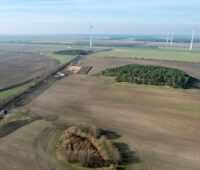 Blick über flaches Land auf einige Windenergie-Anlagen mit hohem Turm und kleinem Rotor.