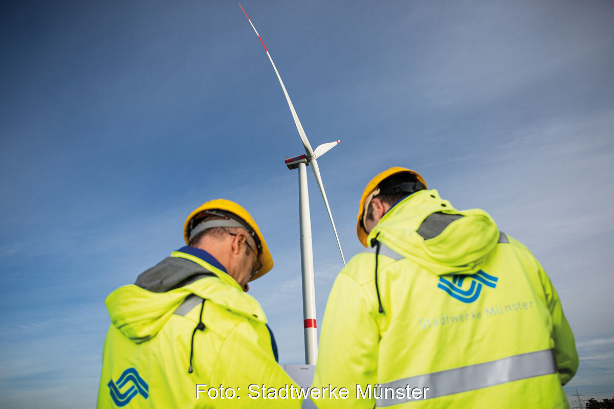Männer in gelber Arbeitsschutzkleidung vor einer Windenergie-Anlage.