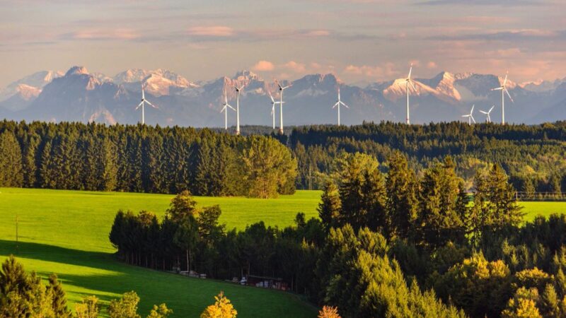 Windenergie-Anlagen in Bayern vor Alpen-Kulisse im Sonnenuntergang