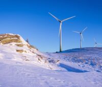 zwei Windkraft-Anlagen auf schneebedeckten Bergen in Österreich