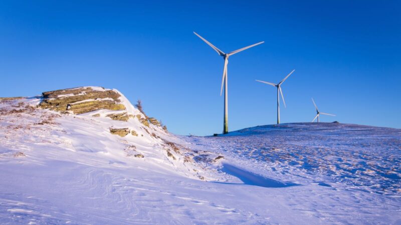 zwei Windkraft-Anlagen auf schneebedeckten Bergen in Österreich