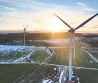 Windräder aus der Vogelperspektive mit Schneeresten auf Äckern und Sonnenaufgang hinter einem Hügel: VSB Frankreich nimmt Windpark Eoliennes de Tortebesse in Betrieb.