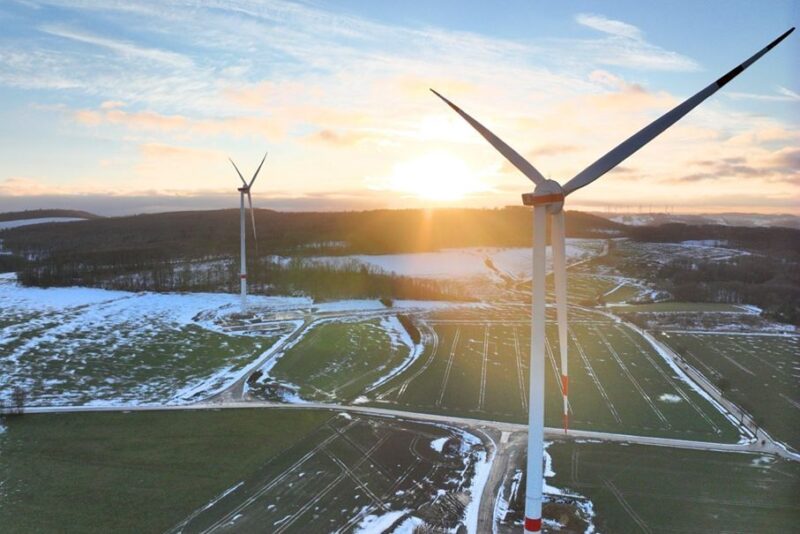 Windräder aus der Vogelperspektive mit Schneeresten auf Äckern und Sonnenaufgang hinter einem Hügel: VSB Frankreich nimmt Windpark Eoliennes de Tortebesse in Betrieb.