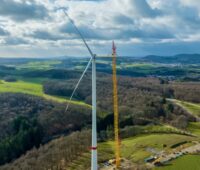 Windenergie-Anlage von Prokon vor Wald und wolkigem Himmel.