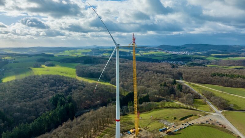 Windenergie-Anlage von Prokon vor Wald und wolkigem Himmel.