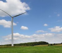 Windkraftanlagen in Wiesenlandschaft mit blauem Himmel und Schäfchenwolken.