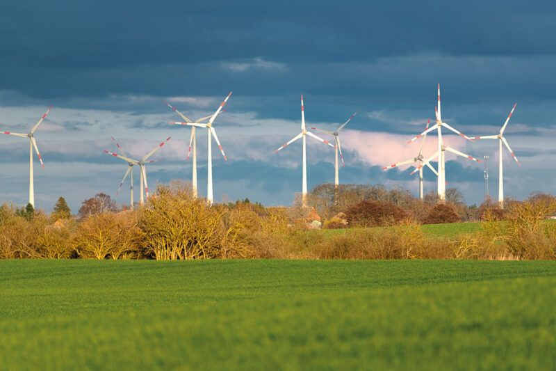 Windpark in Mecklenburg-Vorpommern bei Aprilwetter. Vordergrund: Grünes Getreidefeld, Himmel Dunkle Wolken.