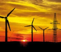 Symbolbild für regionale Vermarktung von Windstrom: ältere Windenergieanlagen mit Strommast im Sonnenuntergang.