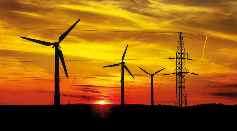 Symbolbild für regionale Vermarktung von Windstrom: ältere Windenergieanlagen mit Strommast im Sonnenuntergang.