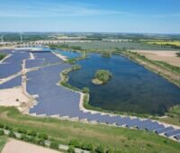 Luftbild einer PV-Freiflächenanlage neben einem See.