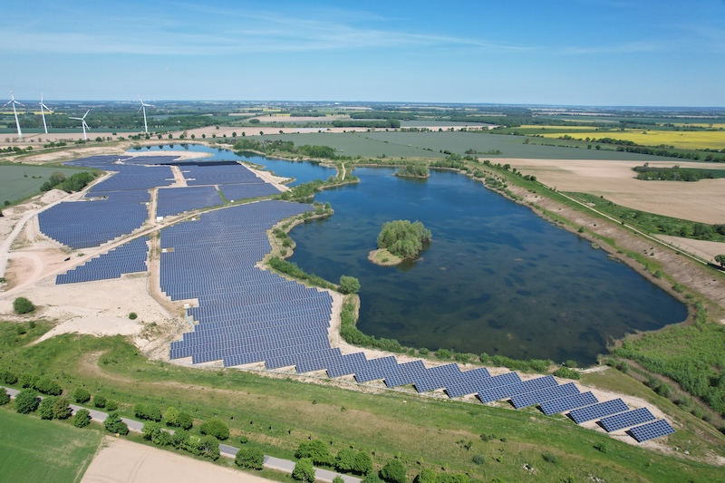 Luftbild einer PV-Freiflächenanlage neben einem See.