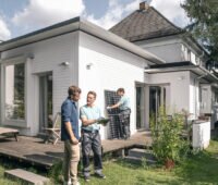 Ein Handwerker spricht mit einem Hauseigentümer vor seinem Einfamilienhaus und Solarmodulen.