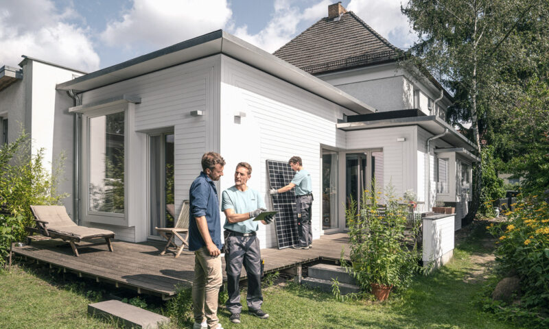 Ein Handwerker spricht mit einem Hauseigentümer vor seinem Einfamilienhaus und Solarmodulen.